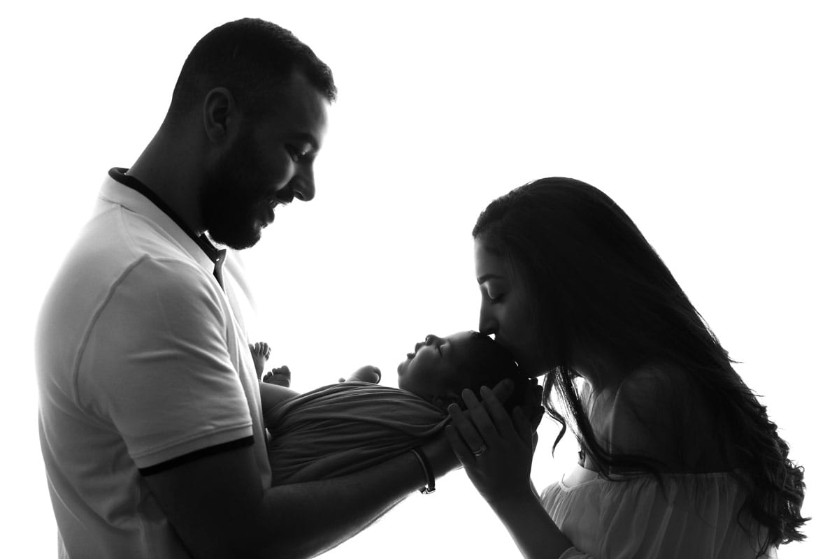 Newborn Shooting Berlin Vater haelt und Mutter kuesst Neugeborenes